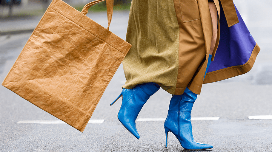 woman wearing blue boots holding a brown shopping tote