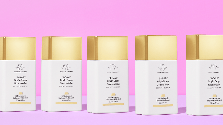 gold and white containers of skin care set on a pink background