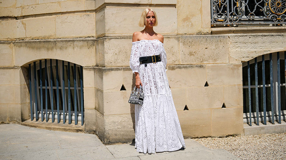 Maria Olympia de Grece wears a white with lace cut-out pattern shoulder-off / puffy long sleeves / long ruffled dress from Dior, a black large Saddle belt from Dior, a black and white embroidered pattern Lady D-Light handbag from Dior, outside Dior , during the Haute Couture Fall/Winter 2023/2024 as part of Paris Fashion Week on July 03, 2023 in Paris, France.