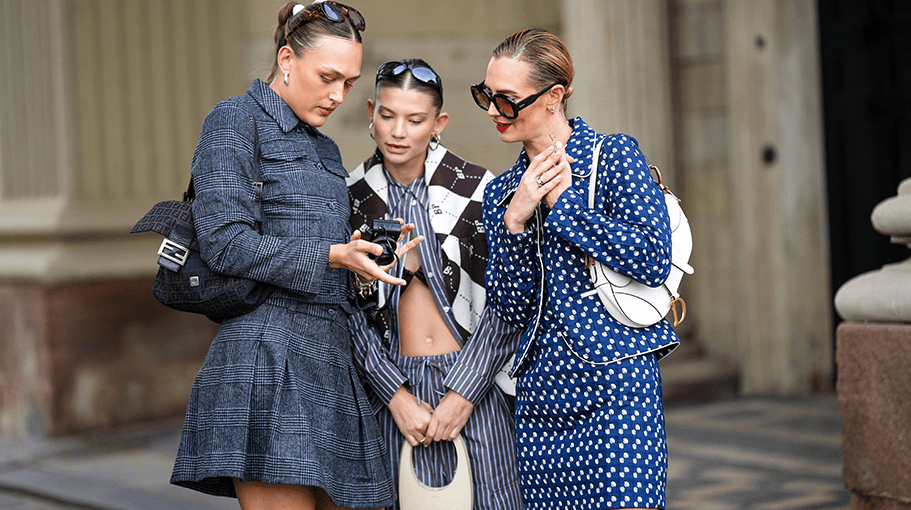 COPENHAGEN, DENMARK - AUGUST 09: A guest (L) wears black sunglasses, a dark gray checkered print pattern buttoned cropped jacket, a matching dark gray checkered print pattern pleated / accordion short skirt, a black shiny leather shoulder bag from Fendi, gold and silver Love bracelet from Cartier, bracelets, silver rings, a guest (M) wears black sunglasses, a black and white checkered print pattern buttoned cardigan, a gray and white striped print pattern shirt, matching gray and white striped print pattern large cotton pants, a white latte matte leather handbag from Coperni, a guest (R) wears black sunglasses, a navy blue with white latte polka dots print pattern silk blazer jacket, a matching navy blue with white latte polka dots print pattern silk short skirt, a white latten matte leather Saddle shoulder bag from Dior, outside Baum und Pferdgarten, during the Copenhagen Fashion Week Spring/Summer 2024 on August 09, 2023 in Copenhagen, Denmark. (Photo by Edward Berthelot/Getty Images)