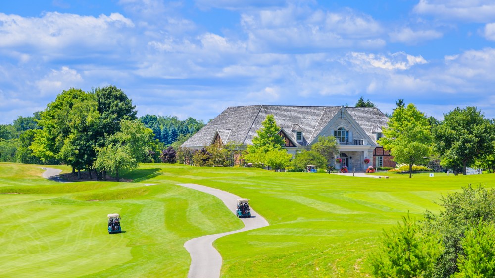 Golf place with gorgeous green and custom built luxury big house on background.