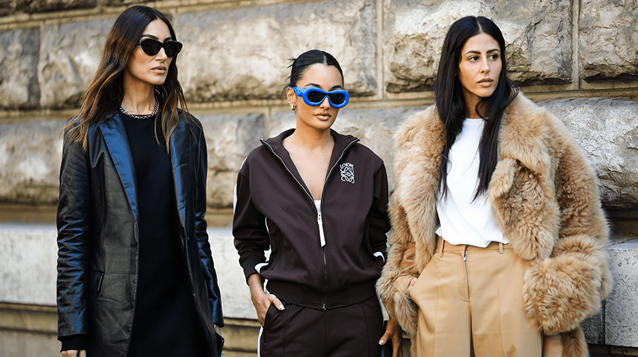 PARIS, FRANCE - SEPTEMBER 30: Giorgia Tordini (L) wears black sunglasses from Loewe, a silver large chain necklace, a black midi long dress, a black shiny leather blazer jacket, a pale blue shiny leather Puzzle handbag from Loewe, silver large shiny leather pattern heels shoes from Loewe, ; Amina Muaddi (M) wears royal blue puffy sunglasses from Loewe, a dark brown with white strap side print pattern zipper sweater from Loewe, matching dark brown with white strap side print pattern flared pants from Loewe, a pale blue shiny leather Puzzle handbag from Loewe, a guest (R) wears a white t-shirt, a brown fluffy long oversized coat, beige high waist large suit pants, outside Loewe, during Paris Fashion Week - Womenswear Spring/Summer 2023, on September 30, 2022 in Paris, France. (Photo by Edward Berthelot/Getty Images)