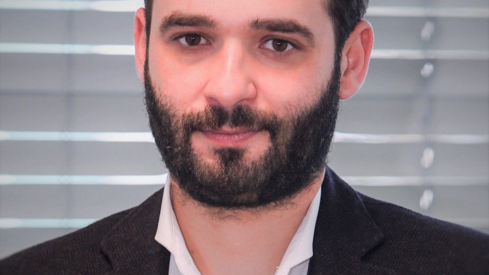 A portrait of ESG tech firm VesselBot's founder and chief executive officer, Constantine Komodromos, wearing a white button-up and charcoal blazer.