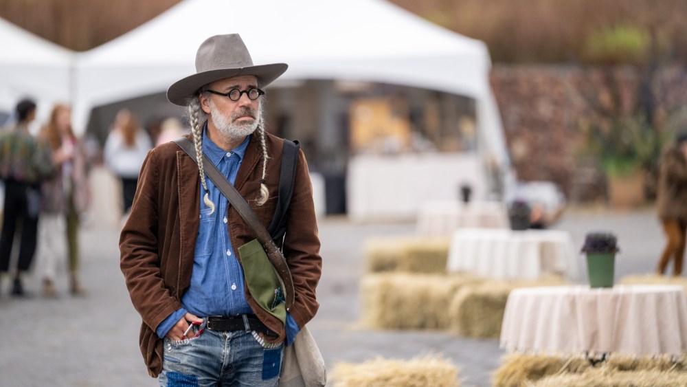 A man with a cowboy hat and braids donning a denim shirt and patchwork jeans with a suede overcoat attending Field + Supply.