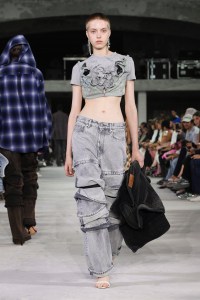 A model wears a cropped T-shirt and layered jeans on the runway at the Y/Project RTW Spring 2024 show.