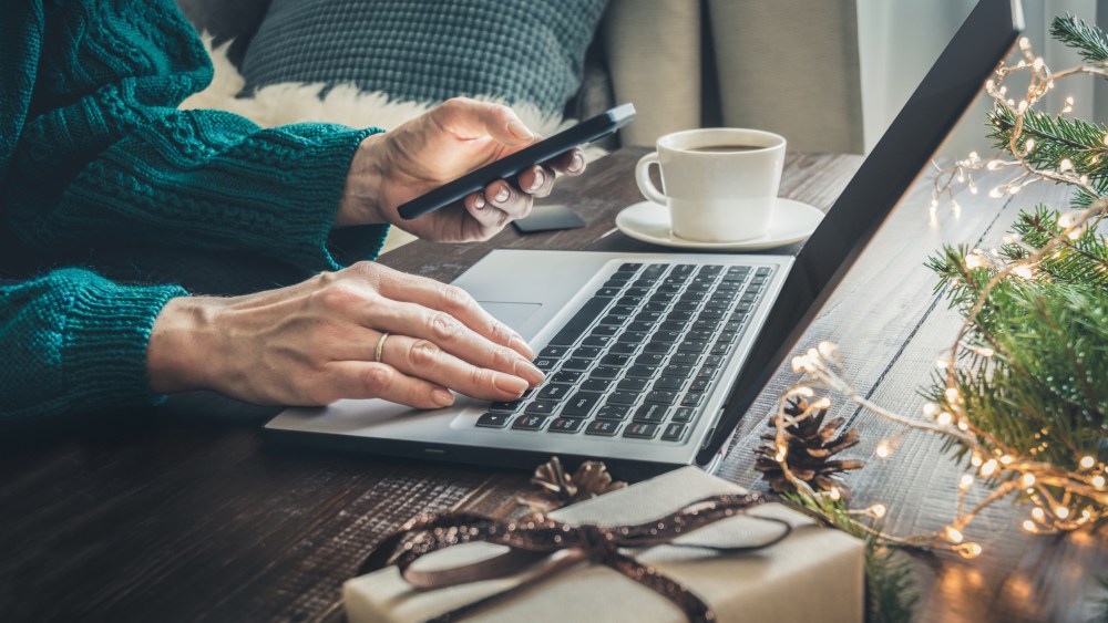 Christmas sales. Woman shopping with smartphone by laptop in home interior. Xmas concept. Planning holidays.
