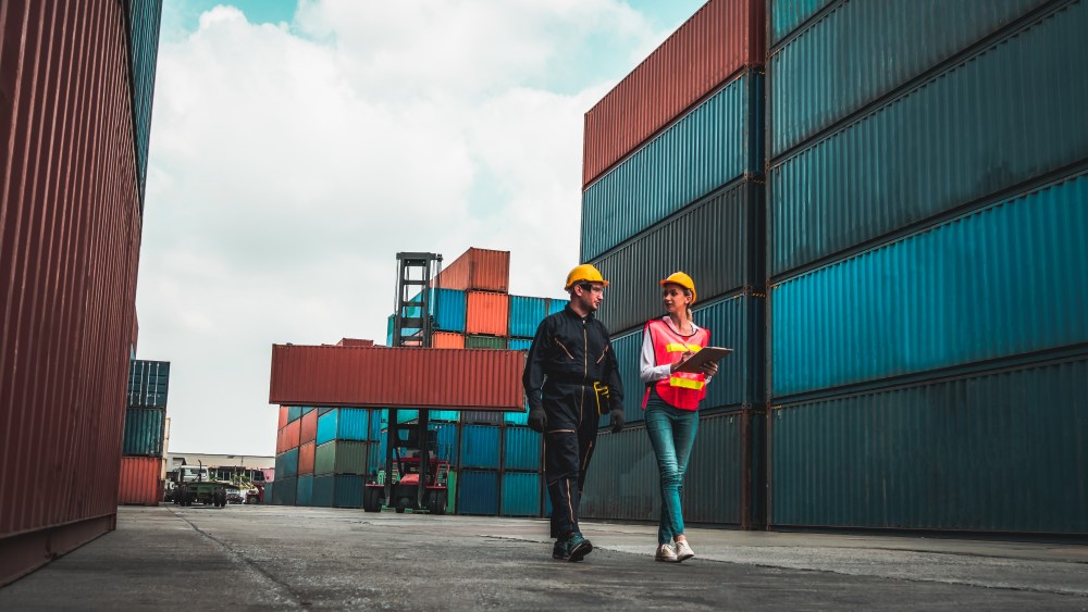 Industrial worker works with co-worker at overseas shipping container yard . Logistics supply chain management and international goods export concept .