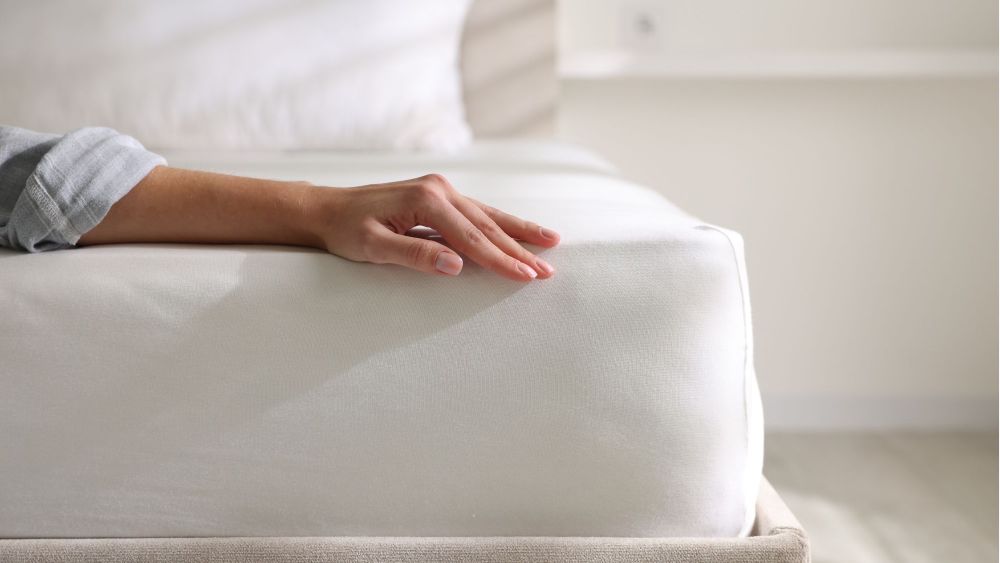 photo of a woman's hand splayed out on a just-made bed with white sheets; best affordable mattresses to shop online