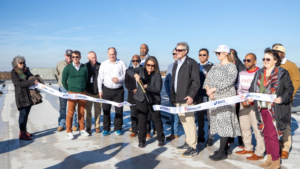 Asics and PowerFlex team members cut co-branded Asics and PowerFlex ribbon on top of roof with solar project in the background.