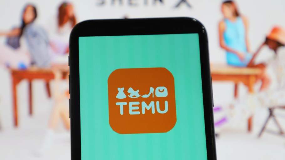The Temu logo displayed on a smartphone with the Shein X mark in the background.