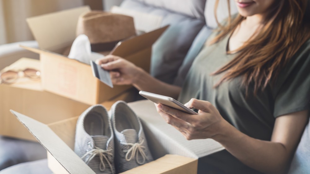 young woman received online shopping parcel opening boxes and buying fashion items by using credit card