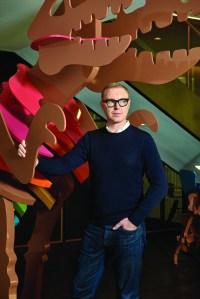 Portrait Stuart Vevers in front of the Rexy dinsaur mascot at Coach's Hudson Yards headquarters