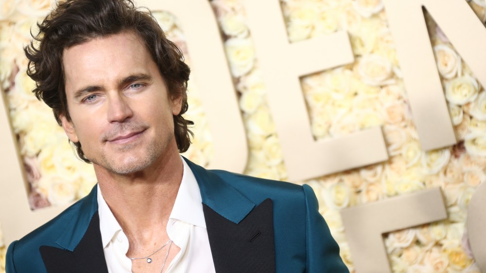 Matt Bomer walking the red carpet with a blue and black suit and white shirt.
