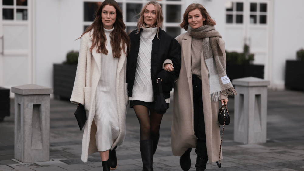 Three women posing for photo on November 15, 2022, in Reykjavik, Iceland, wearing wool coats paired with sweaters, long dresses, and scarves