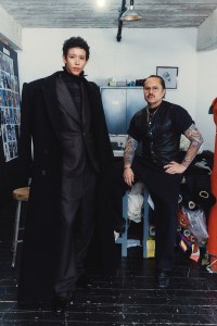 Dilone wears Corpus Christi blouse in wool check, staple blazer in wool houndstooth, Jalisco trousers in wool Glen plaid and double-breasted floor coat in wool and cashmere with Willy Chavarria.