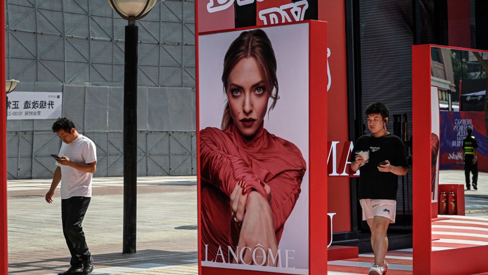 People walk past a billboard for French perfume and cosmetics brand Lancôme at a shopping mall in Beijing.