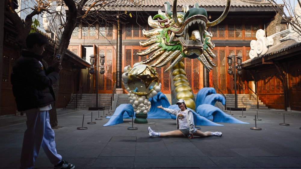 A woman poses for a picture in front of a dragon installation outside a Louis Vuitton store in Chengdu during  Lunar New Year of the Dragon.