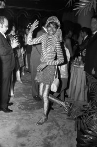 Actress and singer Diana Ross wearing an all metallic outfit with striped top, skirt, leggings and headscarf waving at someone off-camera in Miami, Florida