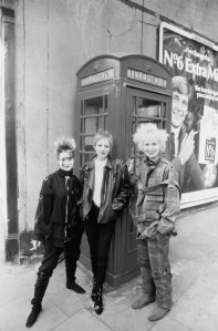 Fashion designer Vivienne Westwood (in plaid) leans against a telephone box with other punk girls on a London street.