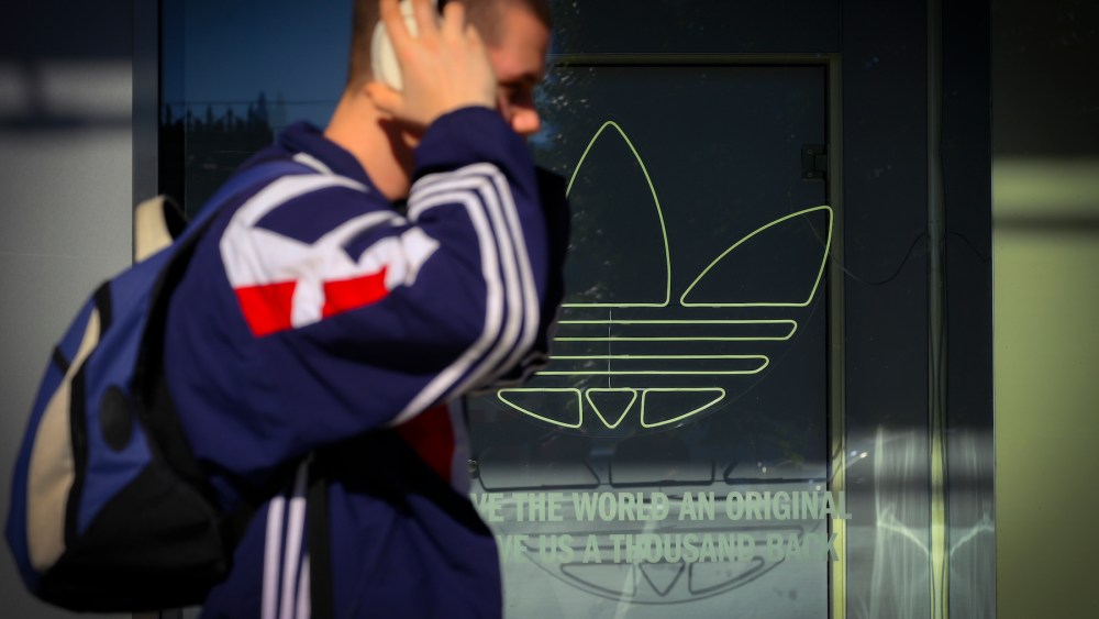 A man in an Adidas training wuit walks past an Adidas logo in a shop window in Warsaw, Poland on 17 May, 2024.