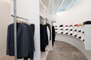 A curved shelf in a menswear zone shelters shoes and hats.