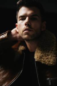 Luke Newton in a leather and shearling jacket by Burberry and an Ami silk tank top.