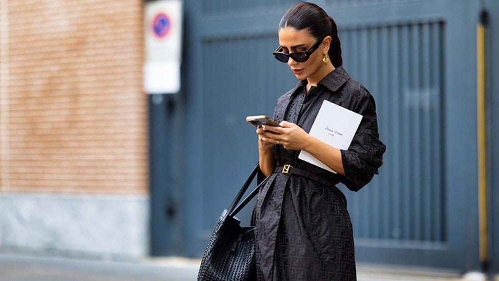 women wearing a black dress and sunglasses looking at her phone