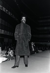 Model Renauld White on the runway at Halston's Fall 1975 Menswear collection debut fashion show. White wears Halston's robe coat in ultrasuede.