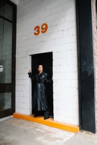 Alexander McQueen leather padded trench coat and wool pinstripe trousers. Givenchy shoes. Tory Burch logo spiked front-back earrings; Spinelli Kilcollin Polaris Blanc ring in 18k gold, two of which are pavé set with full cut white diamonds.