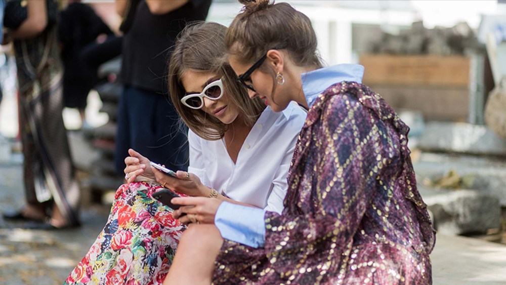 woman wearing a dress checking the phone with a friend outside