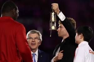 France's swimmer Leon Marchand (C) arrives with the Olympic flame and shows it to athletes and International Olympic Committe (IOC) President Thomas Bach (2nd L) during the closing ceremony of the Paris 2024 Olympic Games at the Stade de France, in Saint-Denis, in the outskirts of Paris, on August 11, 2024.