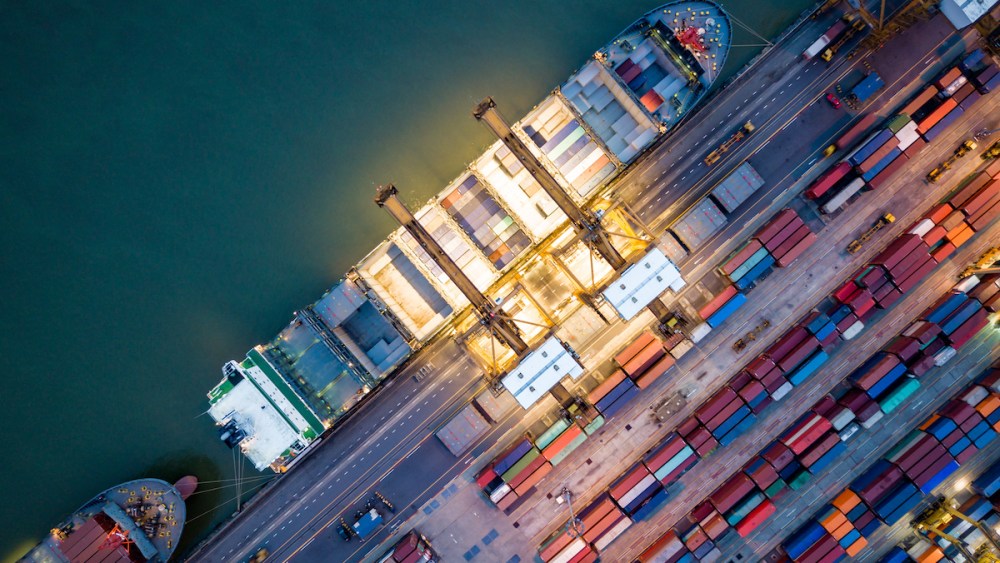 Top view of international port with Crane loading containers in import export business logistics at night.