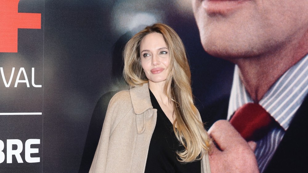 Angelina Jolie wears a camel coat as a cape with a black sweater and skirt.