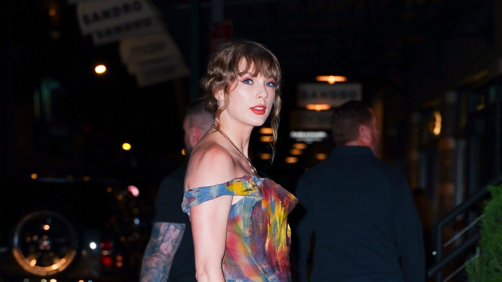 Taylor Swift wears a watercolor red, yellow, and blue off-the-shoulder dress.