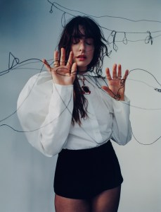 Nina Ricci by Harris Reed cotton poplin puff sleeve shirt; Dior velvet shorts. Commando tights. Bulgari High Jewelry Monete necklace in pink gold with coral elements, 1 bronze coin (Roman Empire, Traianus Aug. - A.D. 98-117), and pavé-set diamonds. B.zero1 18 kt yellow gold three-band ring set with demi-pavé diamonds on the edges, Serpenti Viper one-coil 18 kt yellow gold ring,Serpenti Viper two-coil 18 kt white gold ring set with pavé diamonds