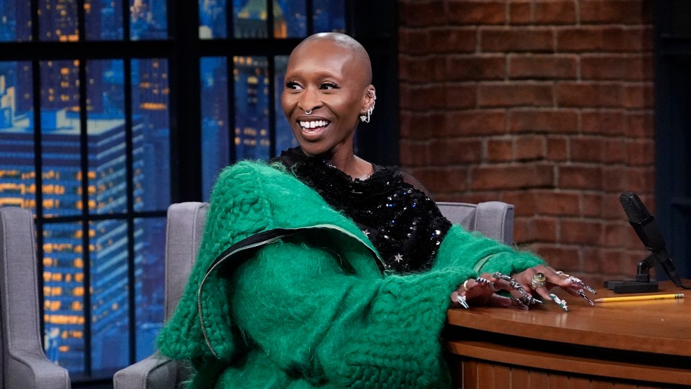 Cynthia Erivo sits in a chair while wearing a green knitted jacket.