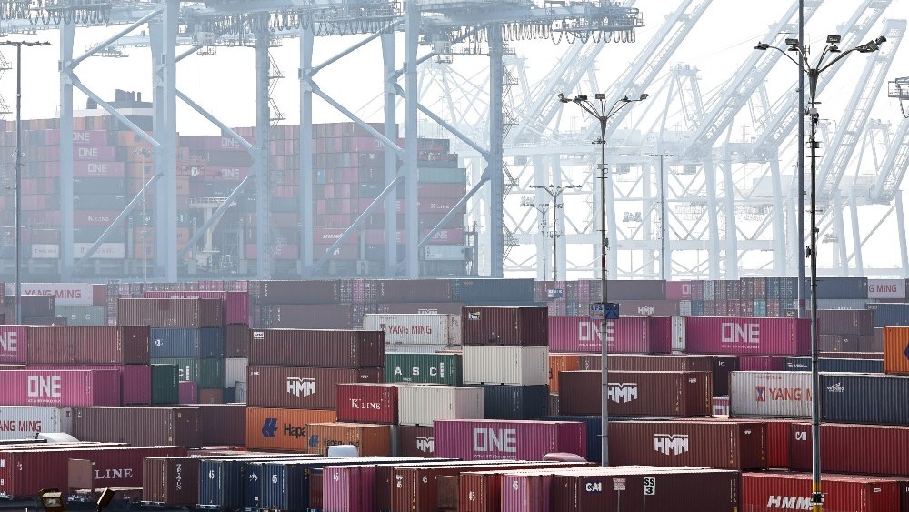 Shipping containers are stacked beneath shipping cranes at the Port of Long Beach on Dec. 4, 2024.