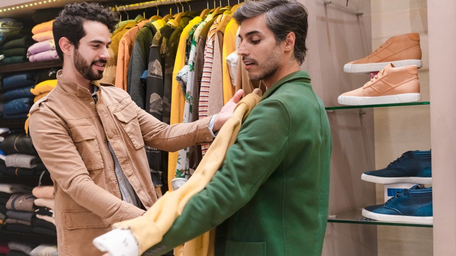 Store owner trying shirt on male customer in menswear showroom