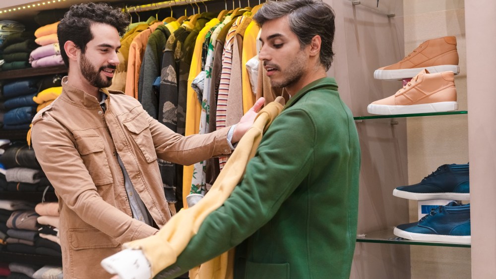 Store owner trying shirt on male customer in menswear showroom