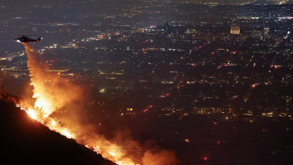 LOS ANGELES, CALIFORNIA - JANUARY 08: A firefighting helicopter drops water as the Sunset Fire burns in the Hollywood Hills with evacuations ordered on January 8, 2025 in Los Angeles, California. Over 1,000 structures have burned, with two people dead, in wildfires fueled by intense Santa Ana Winds across L.A. County. (Photo by Mario Tama/Getty Images)