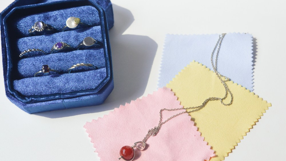 jewelry in a blue velvet case, next to three colors of microfiber cloths over top of which a necklace lays