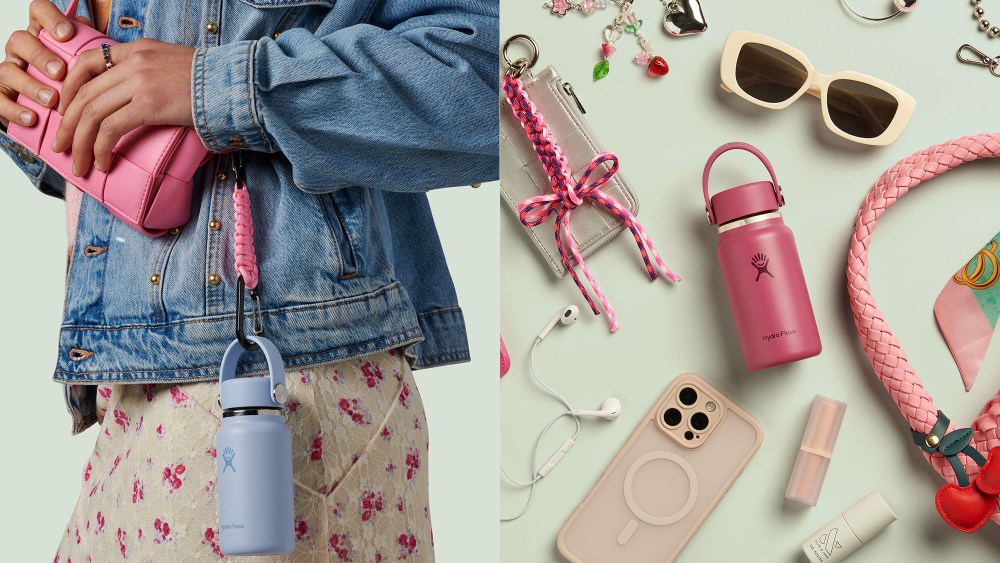 close up of woman holding up a bag that has a little blue water bottle attached to it; pink water bottle amidst accessories like bag charms, phone, sunglasses, and more