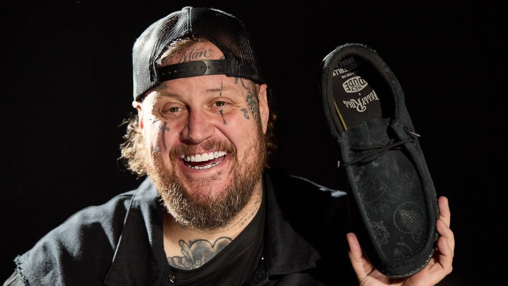 Jelly Roll holding the Jelly Roll x Hey Dude Suede Debossed Shoe.
