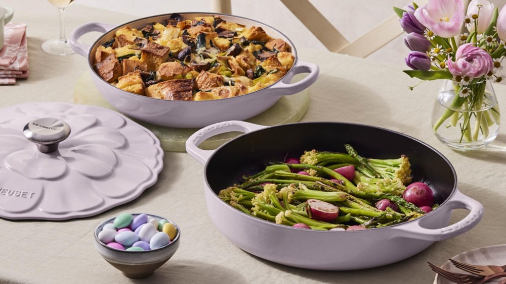 le creuset signature petal braisers in a lilac colorway, resting on a table also decorated with easter eggs, a flower bouquet, and more