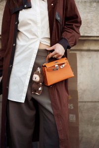 PARIS, FRANCE - MARCH 08: A guest wears brown coat, white blouse, orange Hermes bag with a bag charm brown Labubu monster, grey pants outside the Hermes fashion show during the Womenswear Fall/Winter 2025/2026 as part of Paris Fashion Week on March 08, 2025 in Paris, France. (Photo by Raimonda Kulikauskiene/Getty Images)