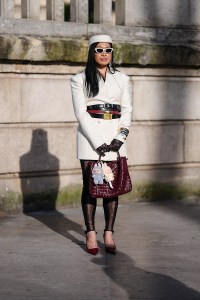 PARIS, FRANCE - MARCH 08: A guest wears white pillbox hat, white sunglasses, cream double breasted blazer jacket, shiny black layered leather belts, burgundy bordeaux leather belt, black bangle bracelet, gold bangle bracelets, black sheer mesh Gucci monogram Gucci gloves, silver rings, burgundy bordeaux woven Bottega Veneta Andiamo leather bag, light blue Labubu bag charm, cream Labubu bag charm, black sheer mesh footless leggings, shiny burgundy bordeaux pointed toe heels leather shoes, outside Elie Saab, during the Paris Fashion week Women's Fall/Winter 2025-2026 on March 8, 2025 in Paris, France. (Photo by Edward Berthelot/Getty Images)