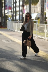 CANNES, FRANCE - MAY 15: Farina Opoku is seen wearing a cropped blazer with lapel collar in khaki green, a white ribbed v-neck t-shirt with black stripes, a small black belt with golden buckle, a black wide leg pleated pants, a pair of white canvas espadrilles with black toe cap and embroidered logo detail from Chanel, round MU52YS sunglasses with golden temples and logo detail from Miu Miu, a Kelly bag 28 Epsom Etoupe in brown leather with gold hardware from Hermès, a pink Labubu monster bag charm, a fine golden necklace with drop shaped diamond pendant from Leo Mathild, a fine golden necklace with round plate pendant, a pair of fine golden hoop earrings from Ariane Ernst Jewelry during day three of the 78th Cannes Film Festival on May 15, 2025 in Cannes, France. (Photo by by Moritz Scholz/Getty Images)