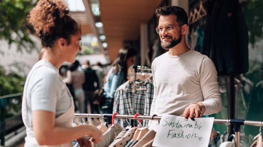 Young entrepreneurs promoting sustainable fashion by selling second-hand clothes at an outdoor market, engaging with customers and highlighting eco-friendly, ethical choices in clothing