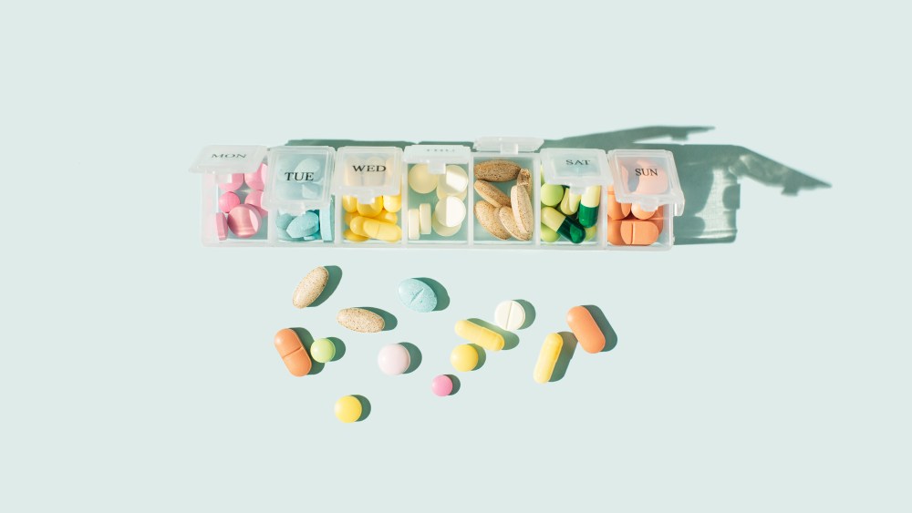 Box for pills and capsules on blue background. Pills organizer with tablets, vitamins, painkillers, medications and dietary supplements. Minimal medical, health care, pharmacology concept. Flat lay, top view.