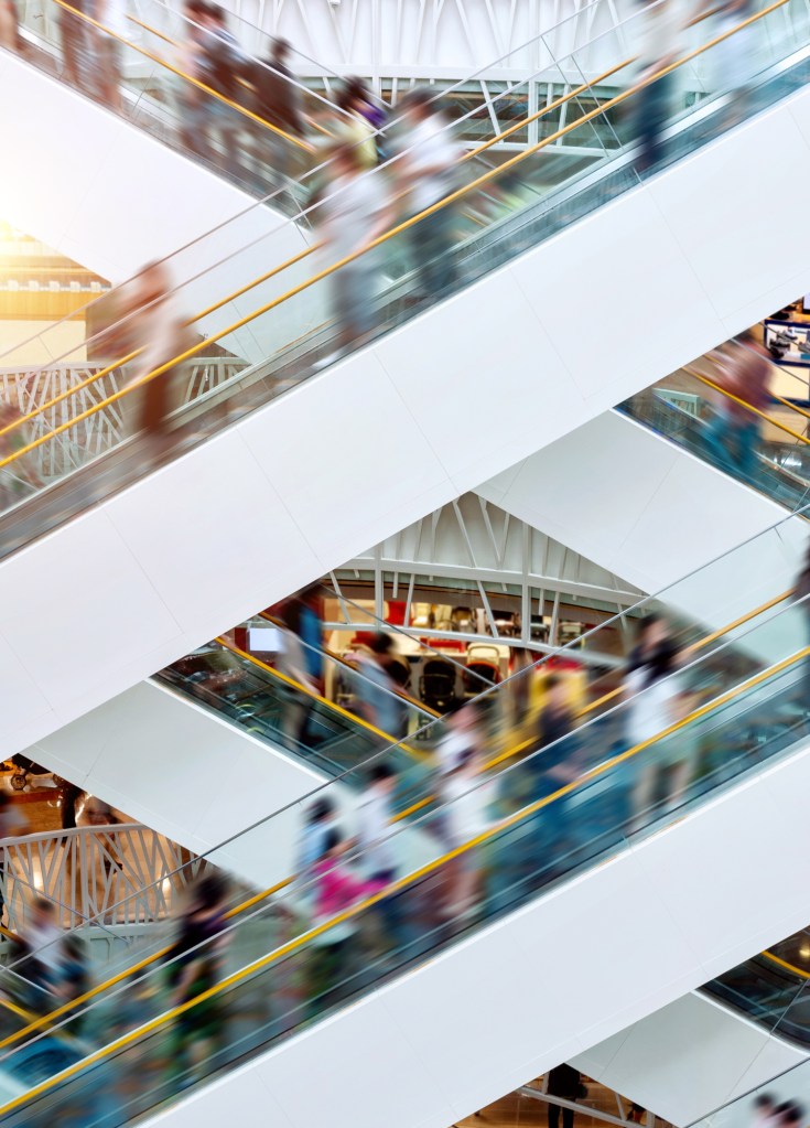 People on many fast moving escalators in modern shopping mall